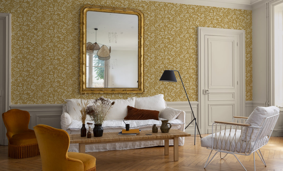 Salon élégant au papier peint floral ocre Libéron Œillet de Reine, avec canapé blanc, miroir doré et parquet.