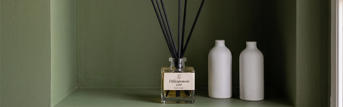 Niche murale avec le diffuseur de parfum d'intérieur à bâtonnets Libéron Délicatement Ciré, deux petits vases en céramique blanche et des murs peints en vert.
