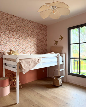 Chambre d'enfant avec soubassement peint en Pêche Cancan 163 Faubourg Libéron, lustre beige, chaise et corbeille en rotin, fenêtre noir et oiseaux dessinés sur le mur.
