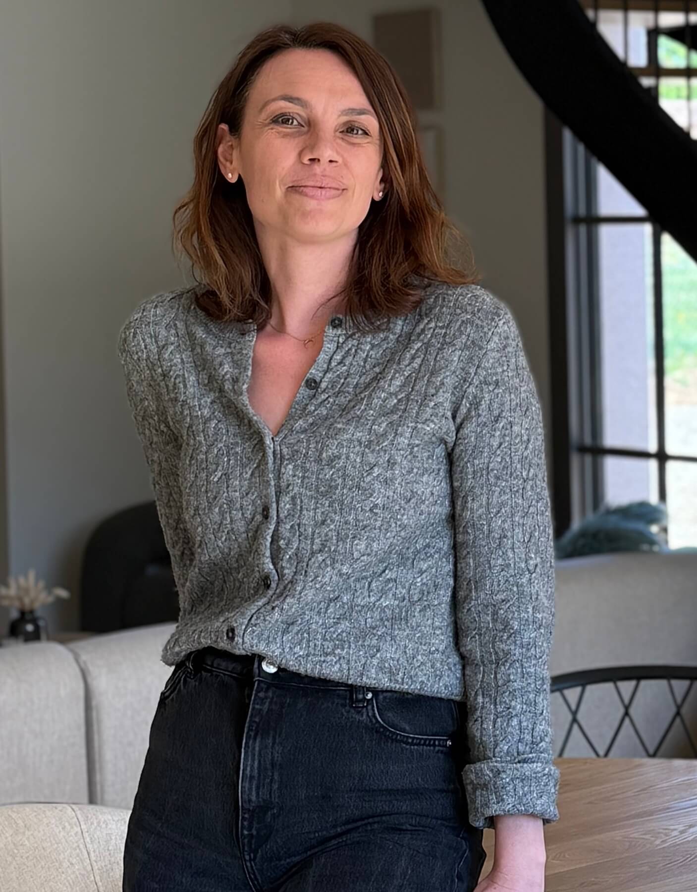 Femme debout dans un intérieur lumineux Libéron, portant un gilet gris et jean foncé, ambiance maison.