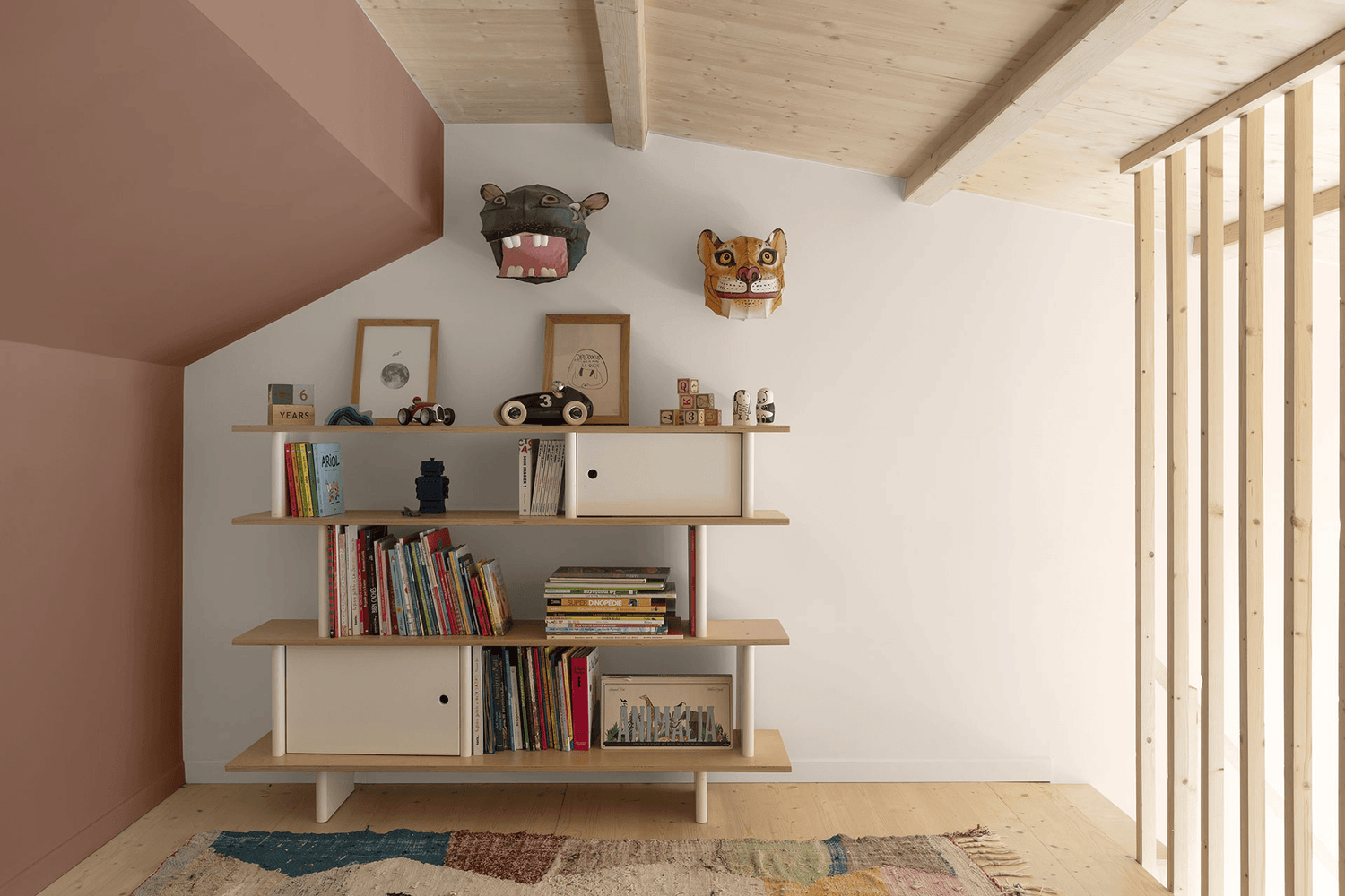 Chambre d’enfant aux murs rose terracotta Libéron, avec bibliothèque, livres et plafond en bois clair.