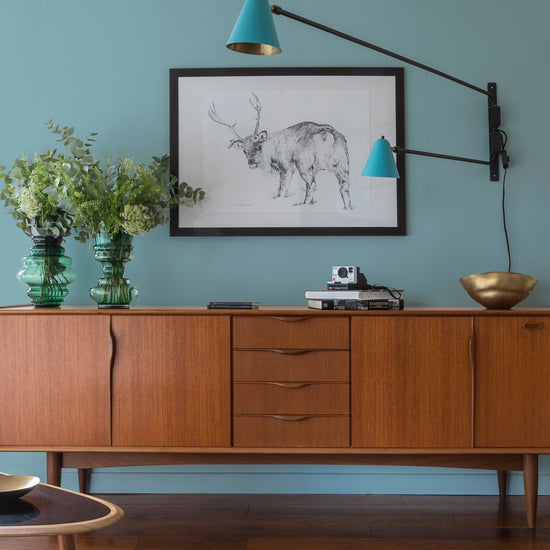 Buffet en bois ciré avec la Cire Black Bison Chataignier Libéron, dans un salon lumineux, avec vases verts, appliques bleues et déco vintage Libéron.