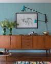 Buffet en bois ciré avec la Cire Black Bison Chataignier Libéron, dans un salon lumineux, avec vases verts, appliques bleues et déco vintage Libéron.