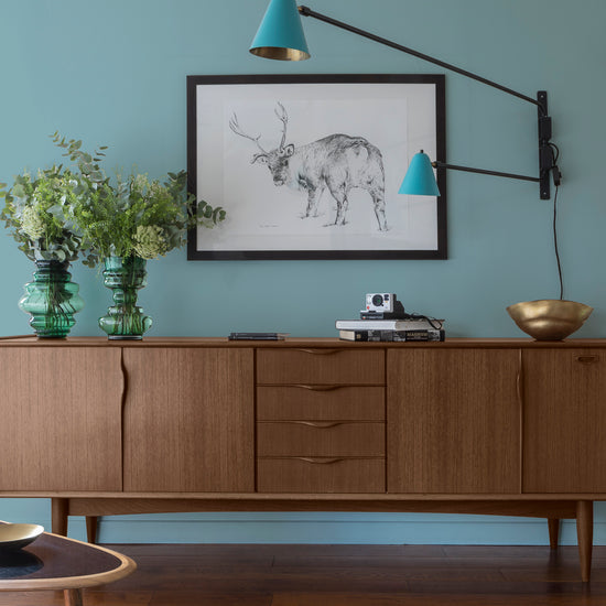Buffet en bois ciré avec la Cire Black Bison Chêne Fumé Libéron, dans un salon lumineux, avec vases verts, appliques bleues et déco vintage Libéron.