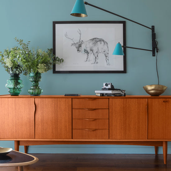 Buffet en bois ciré avec la Cire Black Bison Merisier Foncé Libéron, dans un salon lumineux, avec vases verts, appliques bleues et déco vintage Libéron.