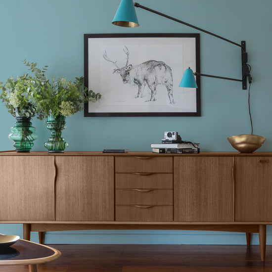 Buffet en bois ciré avec la Cire Black Bison Noyer Libéron, dans un salon lumineux, avec vases verts, appliques bleues et déco vintage Libéron.