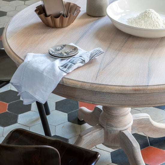 Table ronde en bois cérusé blanc Libéron, avec bol de poudre, linge clair et sol en carreaux graphiques.
