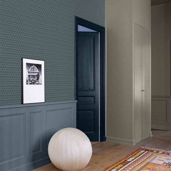 Couloir aux murs bleu grisé et papier peint graphique Libéron Maître Domino, avec boiseries et tapis coloré.
