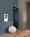 Couloir aux murs bleu grisé et papier peint graphique Libéron Maître Domino, avec boiseries et tapis coloré.