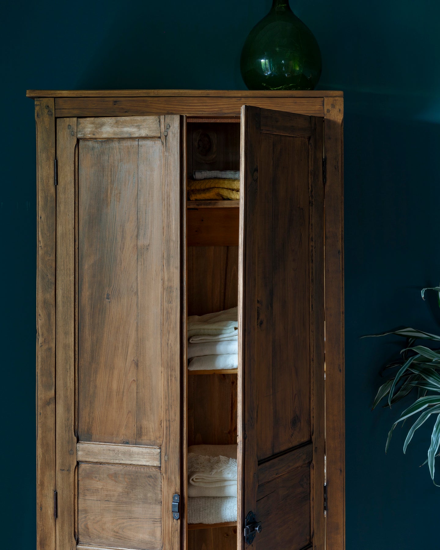 Armoire cirée avec La Crème de Cire teinte Noyer Fumé Libéron, murs bleu foncé, vase vert et plante