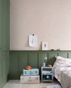 Chambre aux murs Florette Libéron, avec papier peint crème à petit motif vert, soubassement vert sauge, lit clair et valises pastel.