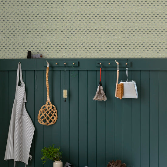 Entrée au mur Florette Libéron, avec papier peint crème à petit motif bleu, soubassement vert foncé, banc en bois et patères.