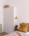 Chambre aux murs rose poudré, avec armoire blanche à panneaux floraux Belle Jeanne Libéron, suspension ocre et linge de lit rose.