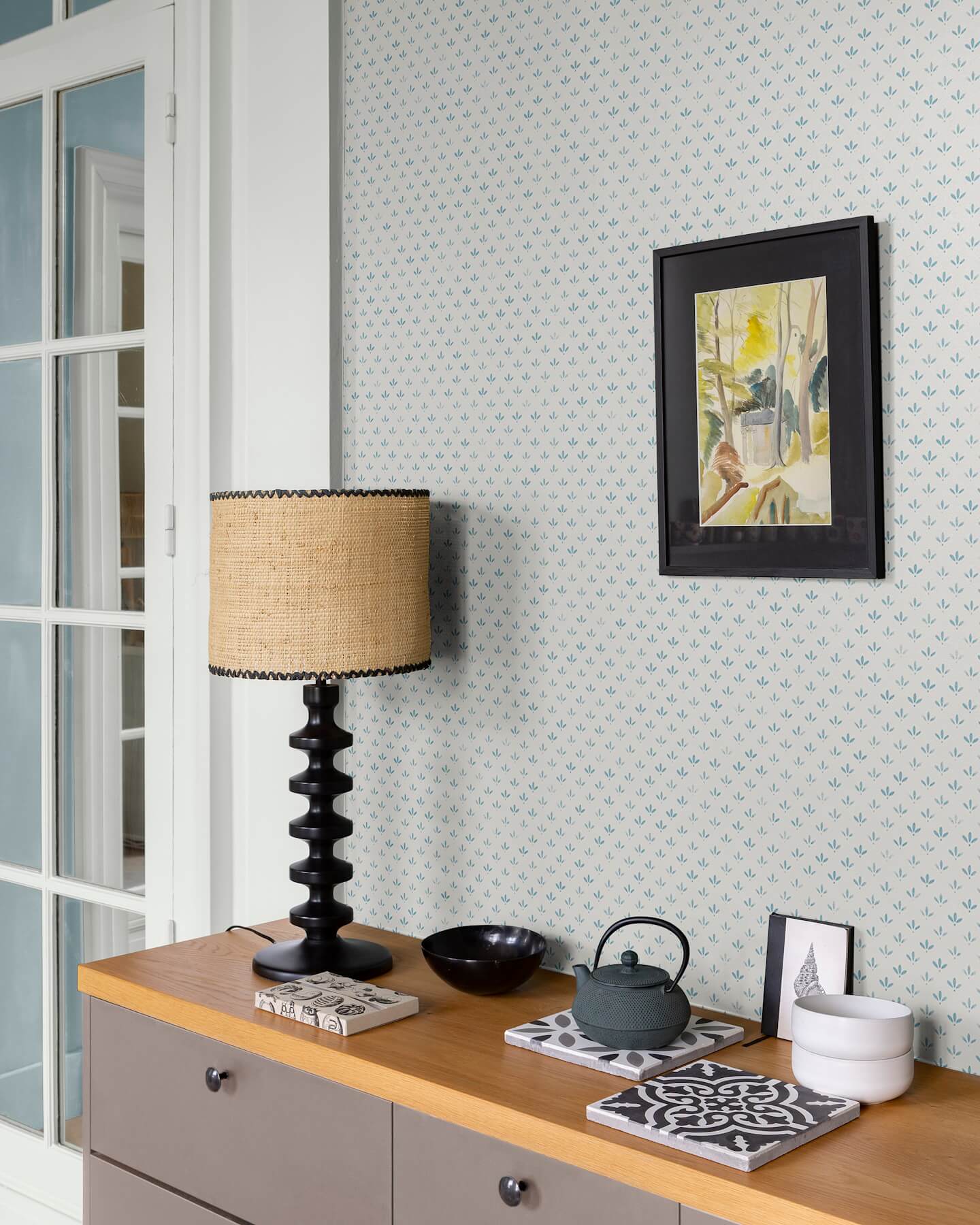 Mur au papier peint Velours de Papier Florette Libéron, avec lampe noire, cadre sombre et meuble en bois clair.