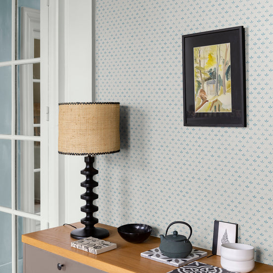 Mur au papier peint Velours de Papier Florette Libéron, avec lampe noire, cadre sombre et meuble en bois clair.