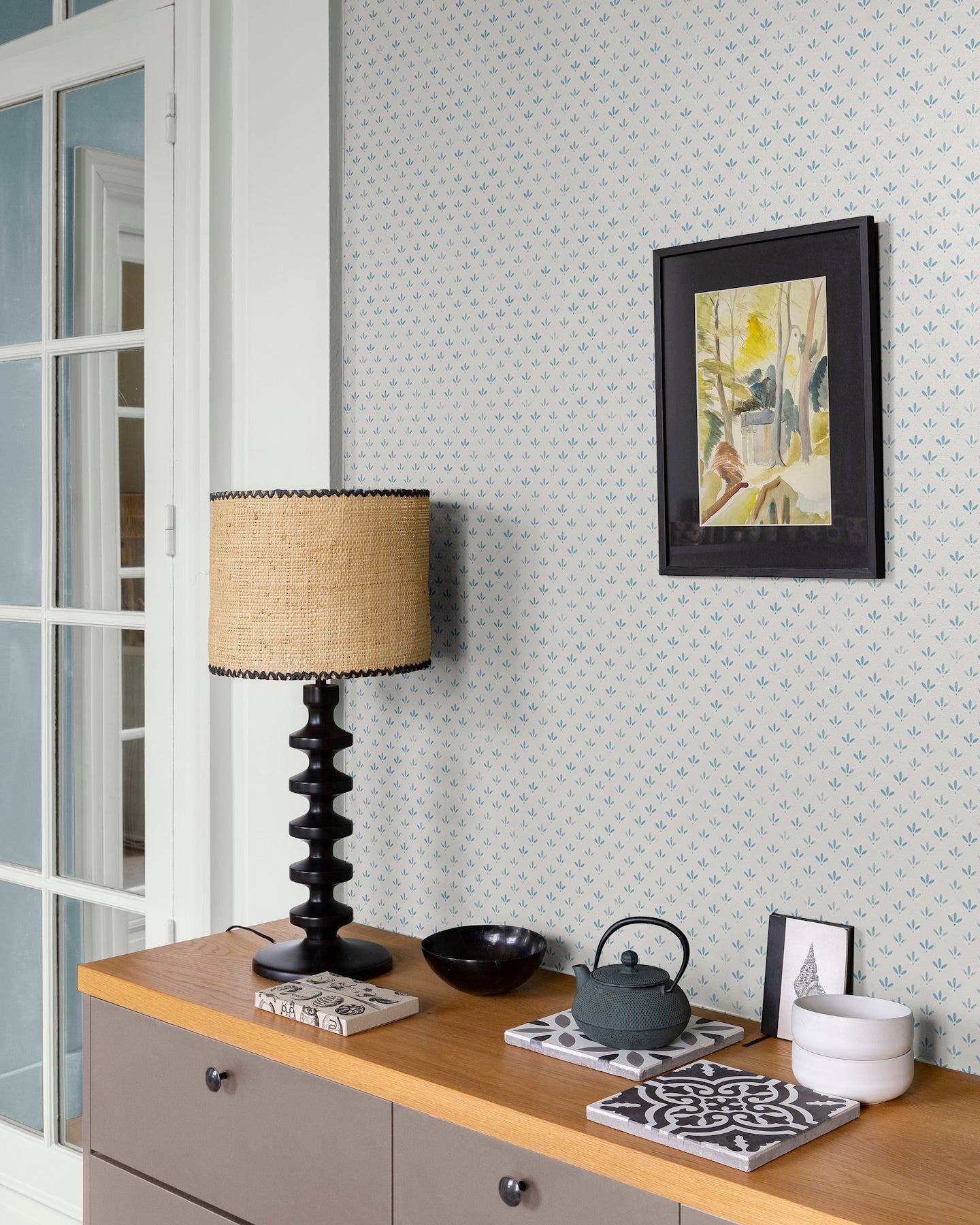 Mur au papier peint Velours de Papier Florette Libéron, avec lampe noire, cadre sombre et meuble en bois clair.