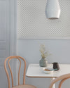 Coin repas aux murs bleu gris et motif géométrique Maître Domino Libéron, avec table blanche, chaises en bois clair et vase.