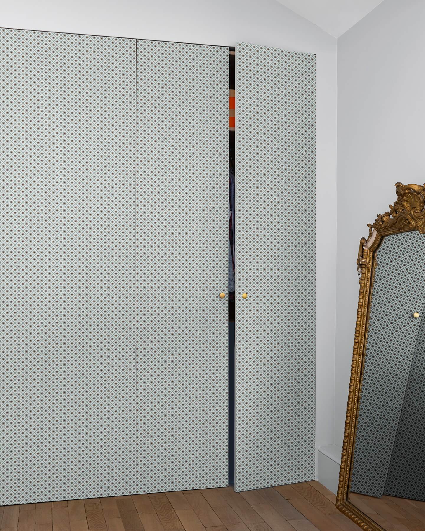 Armoire à motif géométrique Maître Domino Libéron, avec miroir doré posé au sol et parquet en bois clair.