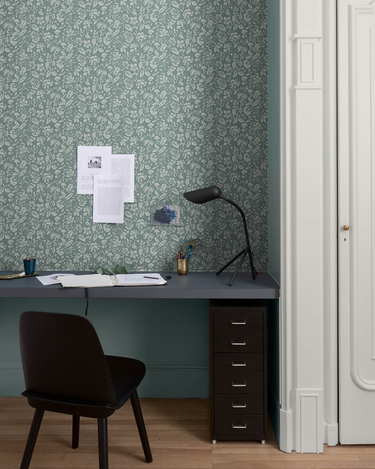 Bureau au mur floral vert d’eau et blanc, teinte Œillet Reine Libéron, avec chaise noire, lampe noire et soubassement bleu.