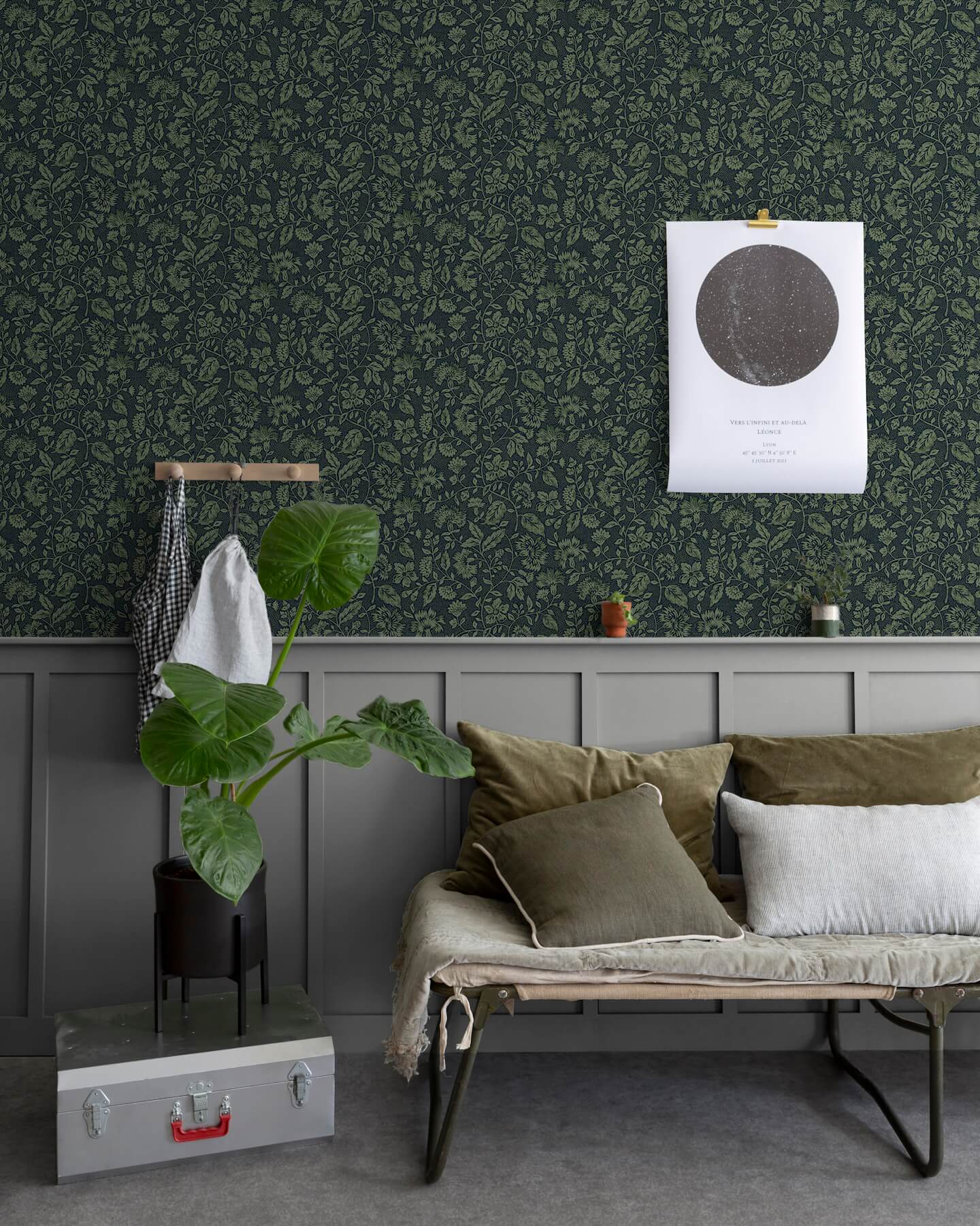 Salon au mur floral sombre, teinte Œillet Reine Libéron, avec banquette kaki, plante verte et soubassement gris.