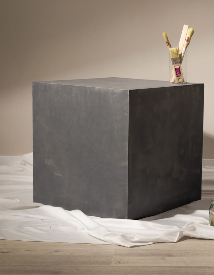 Cube effet béton gris Libéron sur drap blanc, avec pot à pinceaux dans une ambiance atelier.