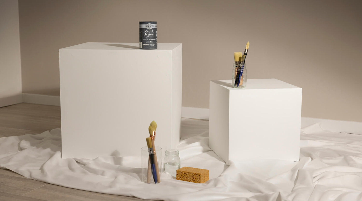 Cubes blancs avant peinture effet béton Libéron, avec pot Meuble signé, pinceaux et éponge sur drap blanc.