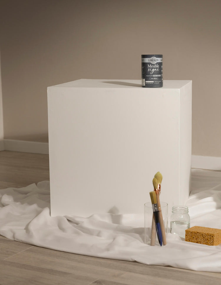 Cube blanc avant peinture effet béton Libéron, avec pot Meuble signé, pinceaux et éponge sur drap blanc.
