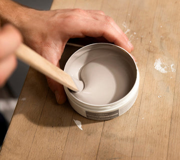 Mélange de la finition effet béton Libéron dans un pot, avec spatule en bois sur table d’atelier.