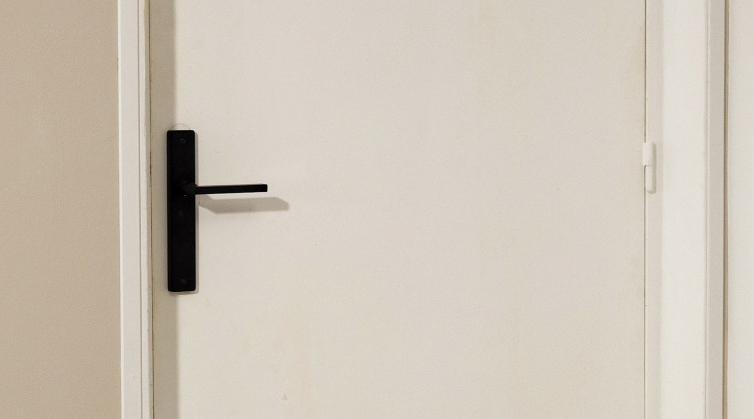 Porte blanche avant peinture effet bois Libéron, avec poignée noire et mur beige.