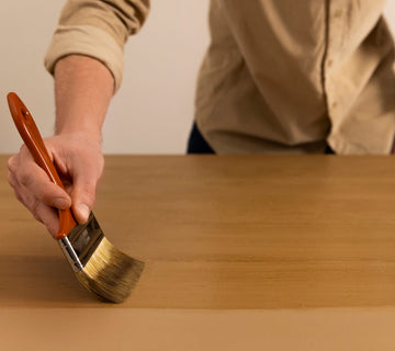 Application au pinceau d’une peinture effet bois Libéron sur une surface beige, avec veinage en cours.
