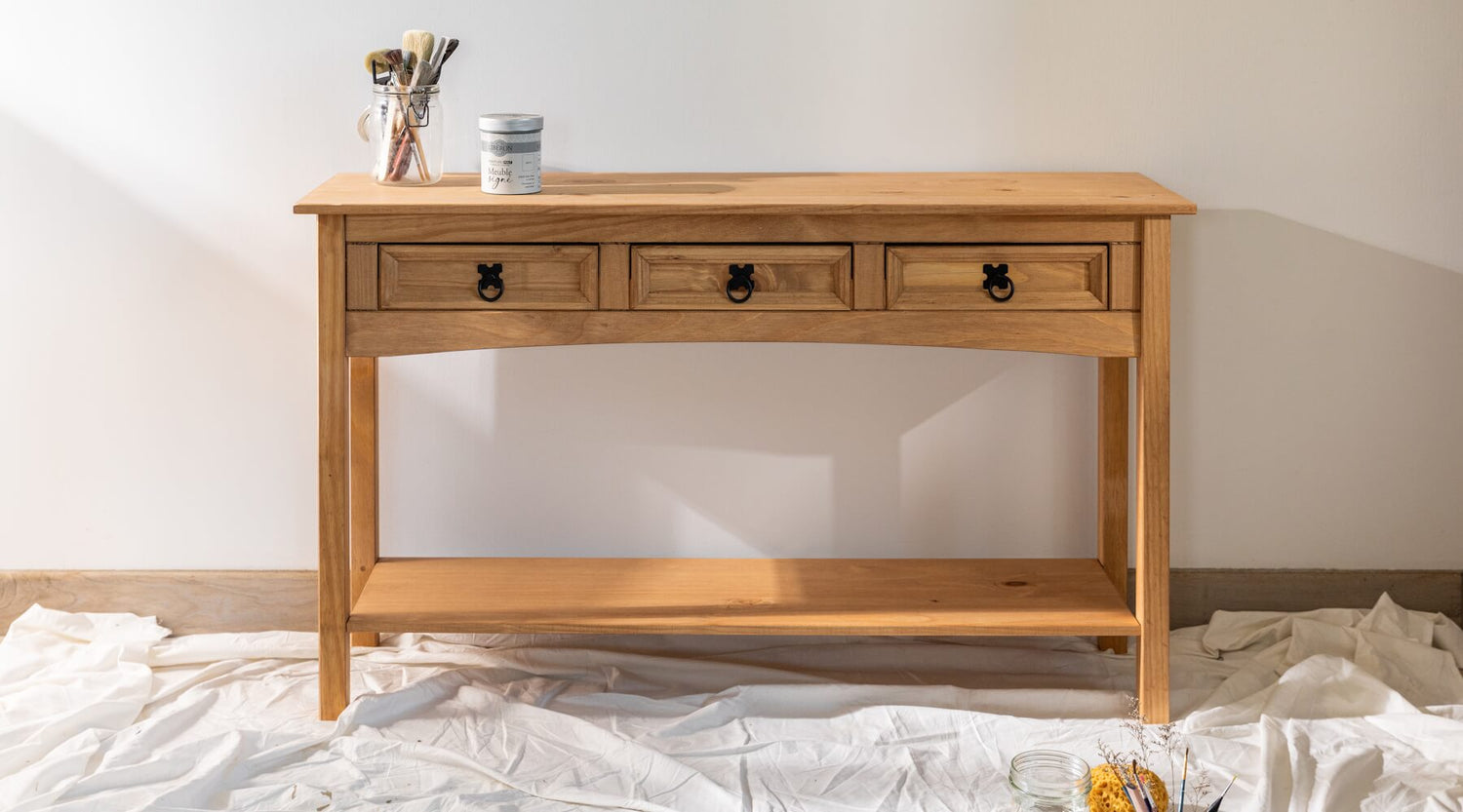 Console en bois avant peinture effet chaulé Libéron, avec pot Meuble signé et pinceaux dans une ambiance atelier.