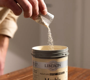 Ajout de poudre effet minéral Libéron dans un pot de peinture, pour préparer la finition décorative.
