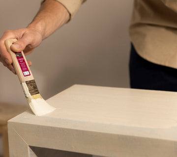 Application au pinceau d’une peinture effet minéral Libéron sur le plateau d’un meuble beige.