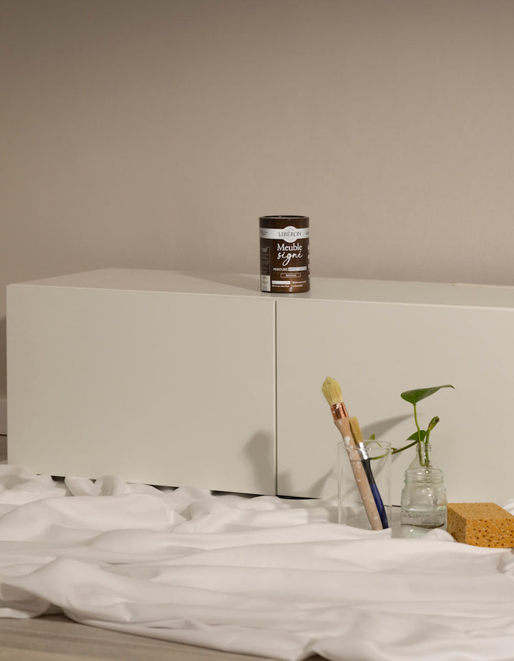 Meuble blanc avant effet oxyde Libéron, avec pot Meuble signé, pinceaux et accessoires de préparation.
