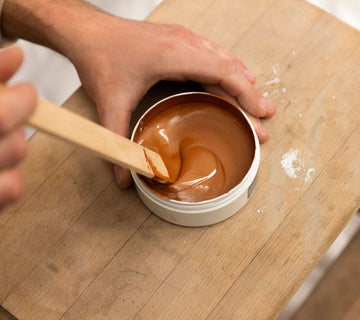 Mélange de la finition effet oxyde Libéron dans un pot, avec spatule en bois sur table d’atelier.