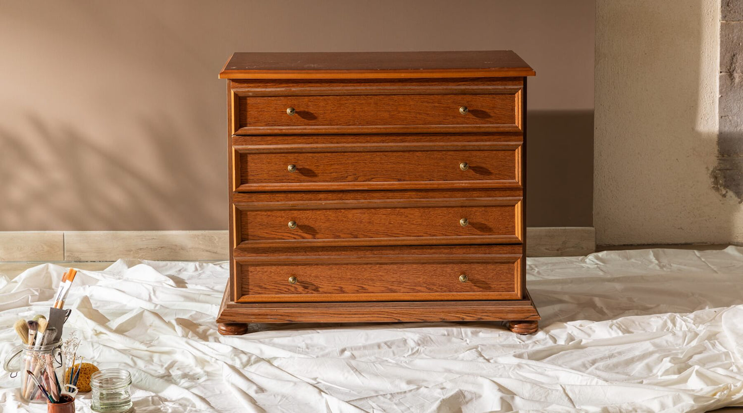 Commode en bois avant effet patiné Libéron, avec accessoires de peinture et toile de protection.