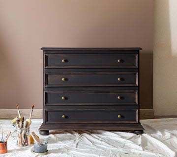 Commode noire effet patiné Libéron, avec boutons dorés, pinceaux et toile de protection.