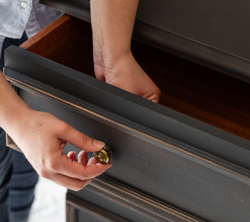 Pose d’un bouton doré sur une commode noire effet patiné Libéron, avec tiroir entrouvert.