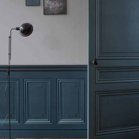 Mur avec soubassement et porte bleu noir Libéron, lampe sur pied noire et parquet en chevrons.