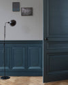 Mur avec soubassement et porte bleu noir Libéron, lampe sur pied noire et parquet en chevrons.