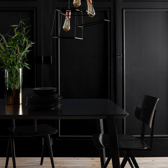 Salle à manger noire avec mur mouluré, table et chaises noires, suspensions graphiques et touches cuivrées.