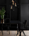 Salle à manger noire avec mur mouluré, table et chaises noires, suspensions graphiques et touches cuivrées.