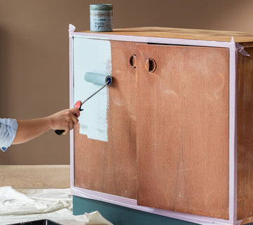 Application au rouleau d’une peinture velours bleu clair Libéron sur les portes d’un meuble en bois.