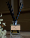 Diffuseur de parfum d’intérieur Libéron Délicatement ciré, flacon en verre avec tiges noires sur parquet.