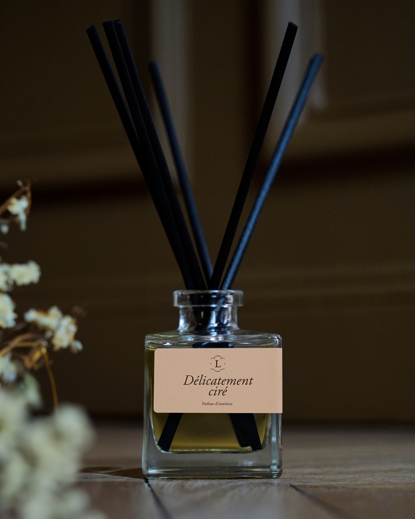 Diffuseur de parfum d’intérieur Libéron Délicatement ciré, flacon en verre avec tiges noires sur parquet.