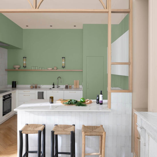 Cuisine vert impressionniste Libéron avec îlot blanc ambré, tabourets tressés et verrière en bois clair.