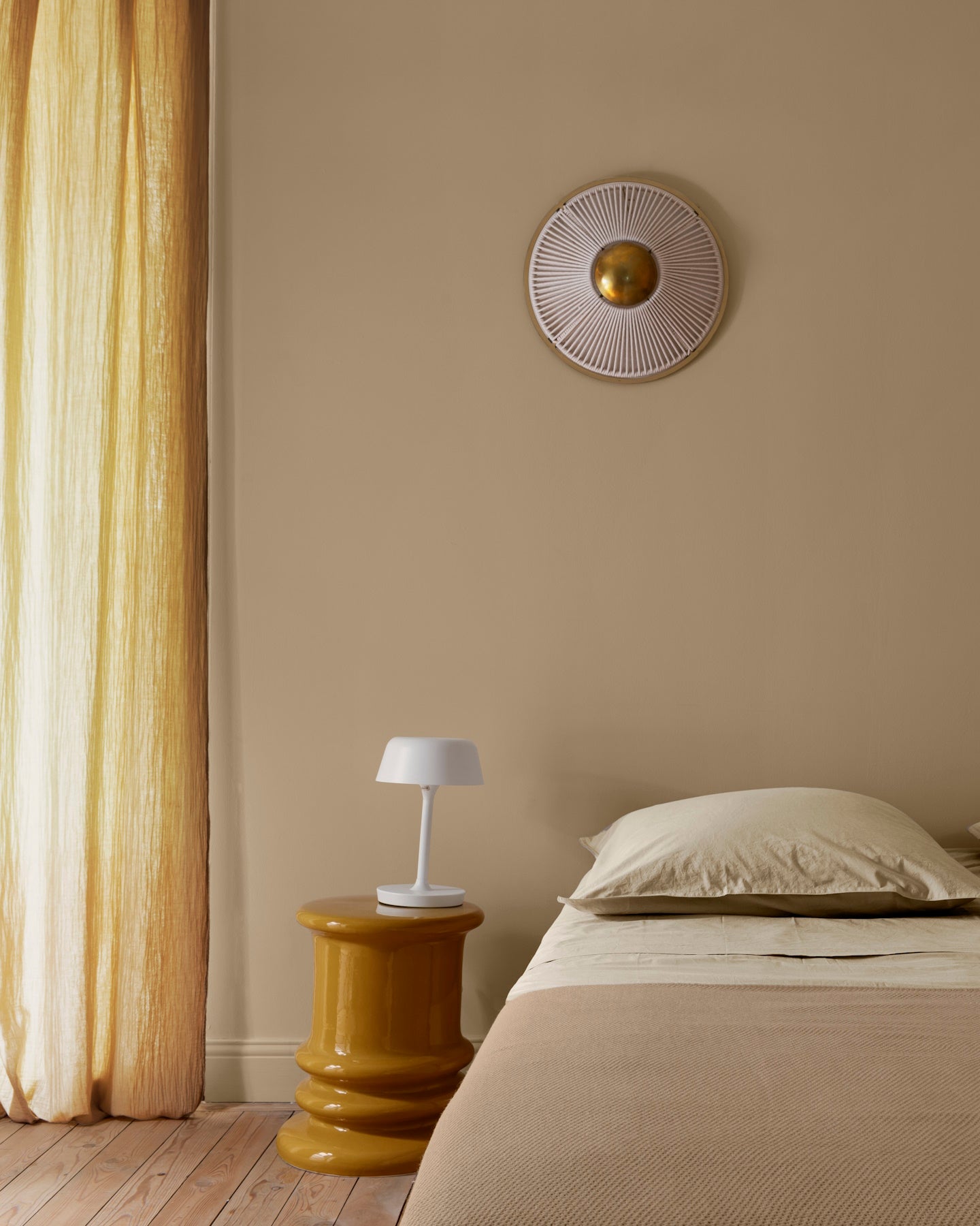 Chambre ambiance chaleureuse avec murs beiges, peinture 163 Faubourg Beige Bottier Libéron, avec rideaux et table de nuit jaunes, et textiles beiges