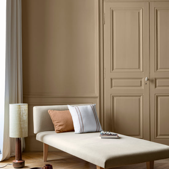 Salon aux murs beige bottier Libéron, avec méridienne écrue, portes assorties, coussins terracotta et parquet clair.