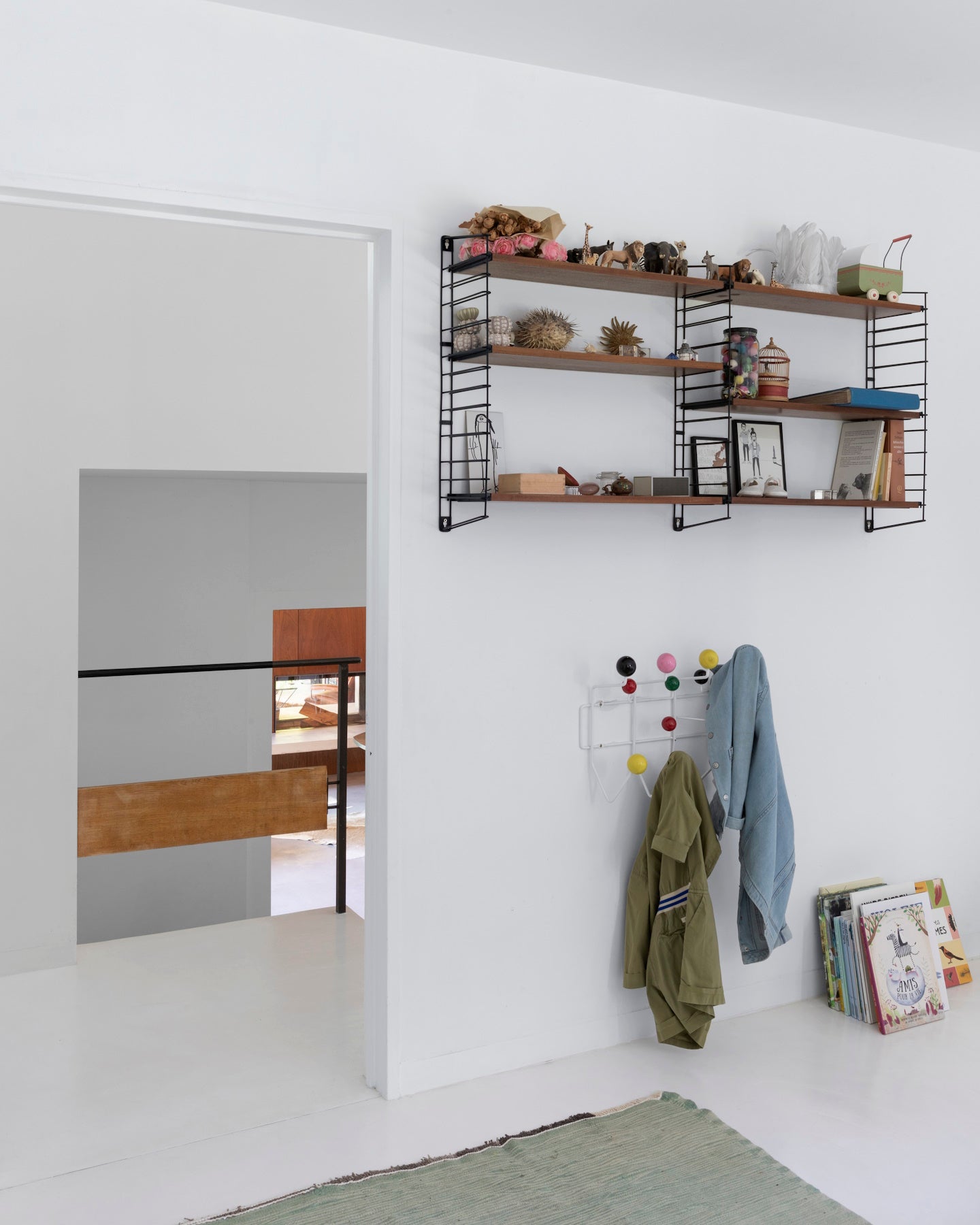 ièce aux murs blanc lingère et blanc art déco Libéron, avec étagères murales, patères colorées et livres.