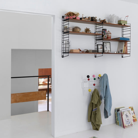 Chambre aux murs blanc lingère et blanc art déco Libéron, avec étagères murales, patères colorées et sol blanc.